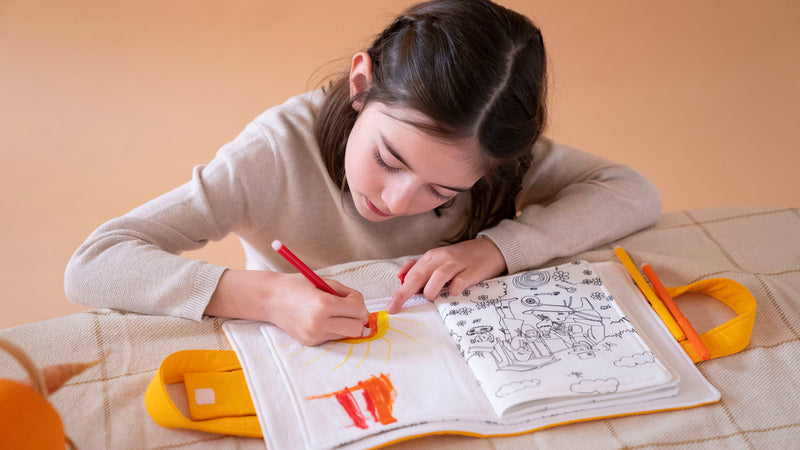 Enfant de 6 ans qui fait un dessin sur la mallette d'activités à colorier lavable 